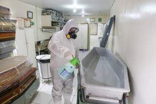 Vestido com roupa anticontágio, agente funerário faz a desenfecção da urna (Foto Paulo Francis)