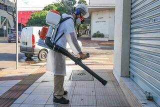 Funcionário faz desinfecção de prédio com solução utilizando alvejante a água sanitária (Foto: Kisie Aionã)