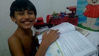 Todo sorridente, Felipe mostra que está lendo seu livro da escola. (Foto: Arquivo pessoal)