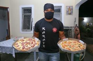 Com máscara, touca e camiseta de karatê, Luciano dos Santos segura as pizzas de calabresa e mussarela. (Foto: Paulo Francis)