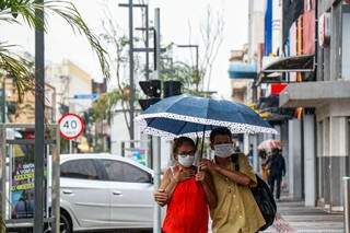 Casal anda pela 14 de Julho se protegendo da chuva e da covid-19 (Foto: Henrique Kawaminami)