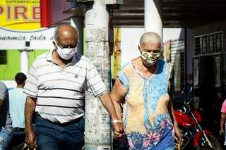 Casal de idosos caminhando de mãos dadas e usando máscaras para se proteger do coronavírus. (Foto: Henrique Kawaminami)