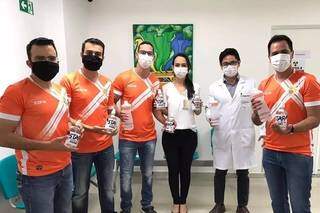 Quatro integrante do time, de uniformes alaranjados, entregando álcool gel para os funcionários do Hospital de Câncer Alfredo Abrão. (Foto: Aquivo pessoal)