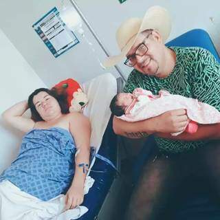Amanda deitada na cama da maternidade e Raphael com a filha recém-nascida nos braços. (Foto: Arquivo pessoal)