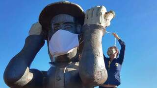 Voluntária colocando a máscara na estátua. (Foto: Franz Mendes) 