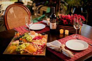 Mesa posta com tábua de frios, guardanapos, taças, vinho, pratos e flores para aquele clima de romance. (Foto: Wilson Jr Fotografia)