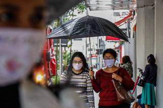 Mulheres se protegem da chuva e também da covid com a utilização de máscaras (Foto: Henrique Kawaminami)