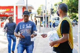 Voluntário entrega máscara para homem sem o item de proteção (Foto: Henrique Kawaminami)