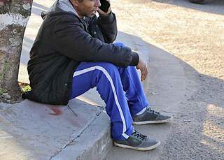 Irmão da vítima chora sentado na calçada próximo ao local onde corpo foi encontrado. (Foto: Kísie Ainoã)