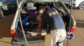 Policial retirando os tabletes de maconha do porta-malas do veículo. (Foto: PRF) 