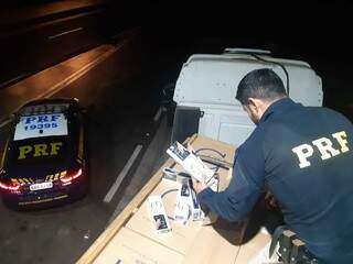 Policial retirando os maços de cigarros de dentro das caixas que estavam na carroceria. (Foto: PRF)