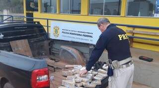 Policial retirando os tabletes de drogas do fundo falso do veículo. (Foto: PRF) 