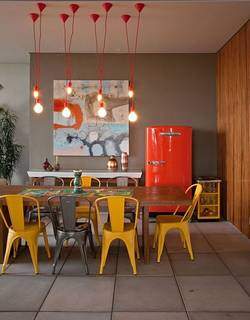 Uso de cores alegres nos móveis e acabamentos torna o ambiente divertido. Como a base é cinza e madeira, foi utilizado cadeira amarela e a geladeira estilo vintage na cor laranja. Bem moderno.