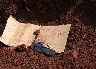 Pedaço de papelão assinado por grupo de extermínio deixado ao lado de corpo; chinelo da vítima foi usado como peso (Foto: Marciano Candia)