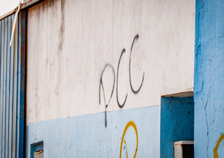 Muro pichado com as iniciais da facção criminosa (Foto: Henrique Kawaminami)