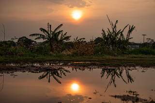 Amanhecer com sol nascendo fraco e poça de água em terrenos baldio no Bairro Amambaí (Foto: Henrique Kawaminami)