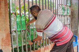 Seu Antônio prendendo uma garrafa no portão (Foto: Silas Lima)