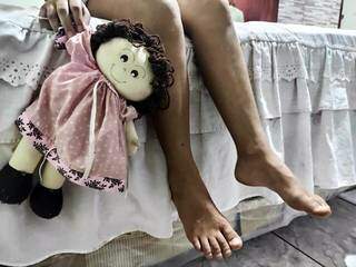 Menina segura boneca em quarto, cena reproduzida para reportagem sobre violência sexual, (Foto: Tainá Jara)