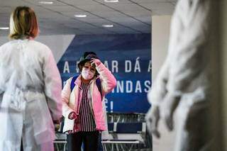 Mulher anda de máscara próxima a profissionais de saúde no Aeroporto Internacional de Campo Grande (Foto: Henrique Kawaminami/Arquivo)