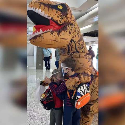Em aeroporto, m&atilde;e recepciona filhos vestida de dinossauro