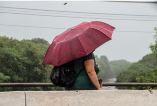 Com guarda-chuva, mulher tenta se proteger que caminha às margens do Rio Anhanduí, tenta se proteger(Foto: Marcos Maluf)