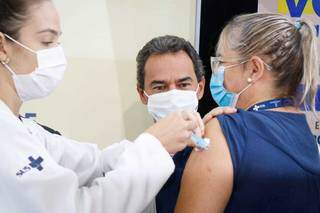 Flávia toma vacina enquanto prefeito observa. (Foto: Henrique Kawaminami)