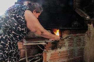 Dona Eva Conceição da Rocha acendendo seu fogão à lenha. (Foto: Marcos Maluf)