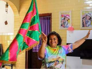 Rose segurando a bandeira da escola em sua casa (Foto: André Bittar)
