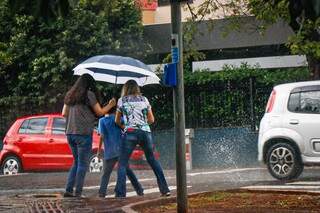 Jovens e criança se abrigam em guarda chuva no Centro de Campo Grande em meio à chuva desta tarde. (Foto: Henrique Kawaminami)