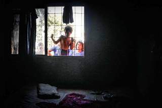 Pela janela, menino olha estragos provocados por incêndio em sua casa. (Foto: Henrique Kawaminami)