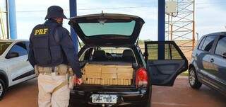 Policial diante dos tabletes de maconha encontrados no porta-malas do veículo. (Foto: PRF) 