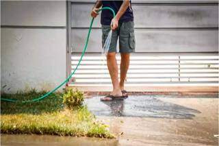 Homem utiliza água da mangueira para lavar calçada (Foto: Henrique Kawaminami)