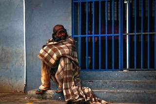 Homem com coberto sentado em escada de lanchonete ainda fechada. (Foto: Henrique Kawaminami)