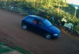 Na imagem é possível ver uma pessoa dentro do carro Pálio segurando um objeto vermelho que lembra um rastelo. (Foto: Reprodução/Vídeo)