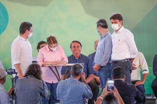 Bolsonaro, de camisa azul, sorri enquanto ministra Tereza Cristina, de camisa rosa, assina documento. (Foto: Henrique Kawaminami)