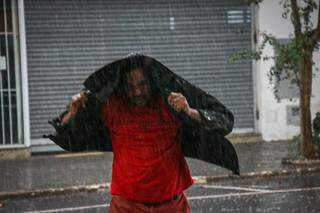 Pego de surpresa, morador de Campo Grande tenta se abrigar da chuva usando jaqueta. (Foto: Henrique Kawaminami)
