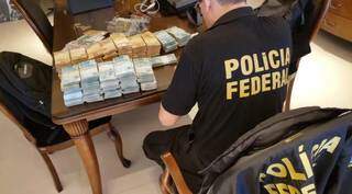 Policial federal conta pilhas de dinheiro em mesa. (Foto: Divulgação)