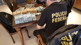 Policial analisando dinheiro apreendido pela manhã. (Foto: Polícia Federal)