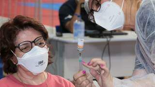 Profissional de saúde mostra dose de vacina em seringa para mulher (Foto: PMCG)