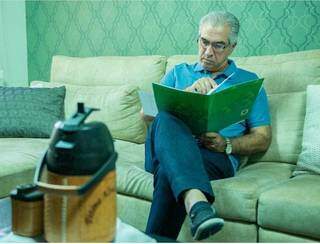 Governador Reinaldo Azambuja (PSDB) lendo documento sentado no sofá de casa. (Foto: Reprodução/Instagram)