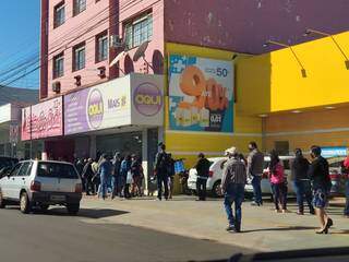 Pessoas em fila que dobra esquina para atendimento no centro de Dourados (Foto: Helio de Freitas)