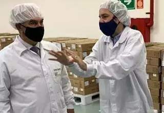 O governador Reinaldo Azambuja, à esquerda na foto, ouve explicações de executivo em fábrica que vai fazer a Sputnik no Brasil, durante visita em abril. (Foto: Divulgação)