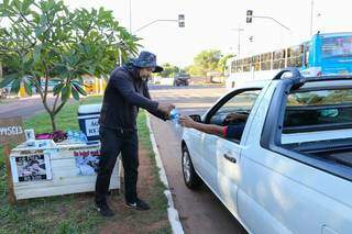 Rafael vendendo uma água à motorista que passa pela avenida (Foto: Paulo Francis)
