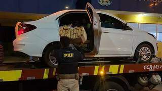 Policial ao lado do carregamento de maconha encontrado no veículo. (Foto: PRF)