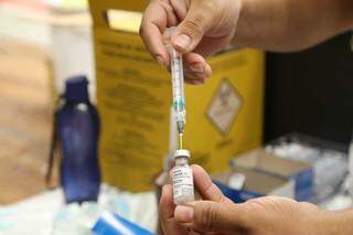 Profissional de saúde segura ampola de vacina e injeção que será aplicada (Foto: Arquivo/Campo Grande News)