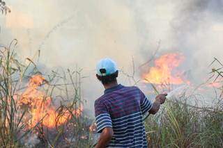 Morador usando mangueira para controlar chamas em vegetação. (Foto: Henrique Kawaminami)