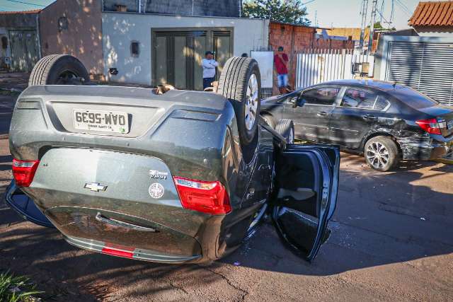 Motorista bate na traseira de carro estacionado e capota em avenida 