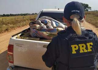 Policial ao lado do veículo onde foram encontrados os tabletes de maconha. (Foto: PRF)
