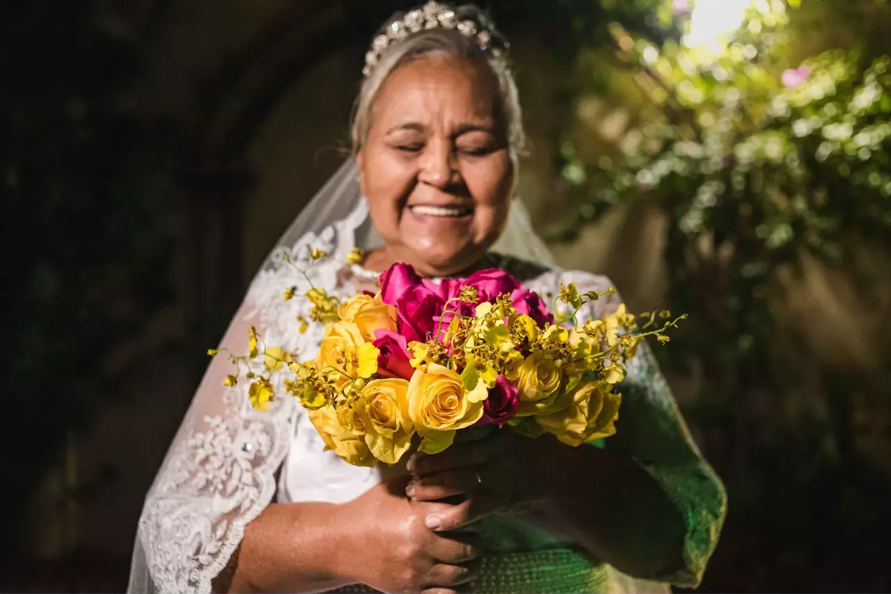 De véu e grinalda, Maria sorri segurando o buquê com rosas amarela e rosa. (Foto: Roberto Simões)