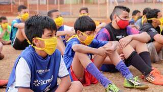 Meninos, com máscara, recebem instruções em escolinha. (Foto: PMCG)